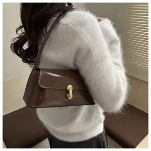 Close-up of glossy brown faux leather baguette bag with gold buckle on white sweater