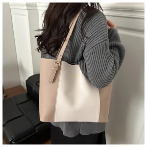 Detail shot of a beige and khaki color-block tote bag worn by a model in a minimalist room
