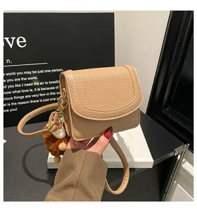 Close-up of beige lychee textured leather crossbody bag with chain strap and fur pompom