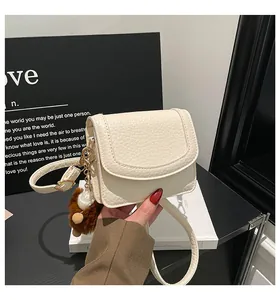 Macro shot of off-white lychee texture leather bag with gold chain and teddy bear charm