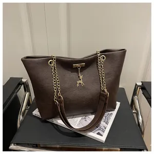 Detail of dark brown tote bag featuring golden chain strap and iconic deer charm pendant