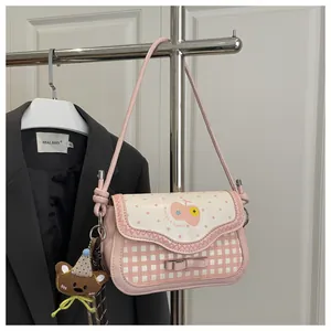 Detail of pink plaid handbag featuring a cartoon apple print and a plush bear keychain