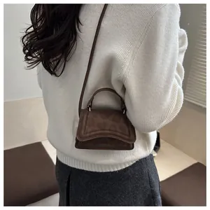 Close-up of a small brown suede handbag with wave-cut flap and animal texture on a model