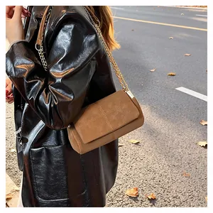 Gros plan du sac en daim marron avec surpiqûres en croix et chaîne dorée chic