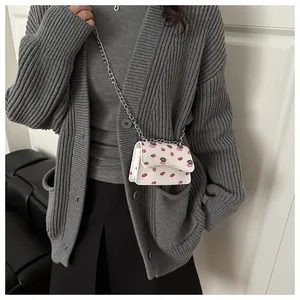 Nahaufnahme einer weißen Mini-Kettentasche mit roten und lila Lippenmustern am Model