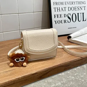 Chic beige lychee textured shoulder bag with plush monster charm on wooden table