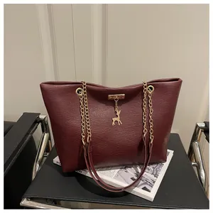 Detail of burgundy textured leather tote bag with gold chain strap and deer charm