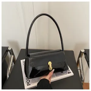 Detail of glossy black patent leather baguette bag with a metallic gold cylinder clasp