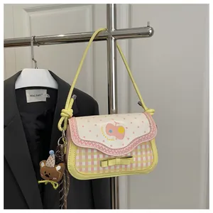 Close-up of yellow plaid bag with apple print flap and cute brown bear plush charm