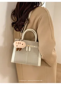 Detalle de bolso tote de ante gris y blanco con colgante rosa sobre abrigo de lana