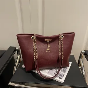 Large burgundy tote bag with gold chain strap and deer pendant on a stylish chair