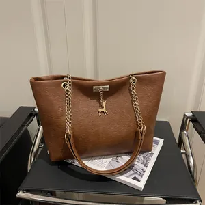 Brown frosted tote bag with gold chain strap and deer charm on a leather seat