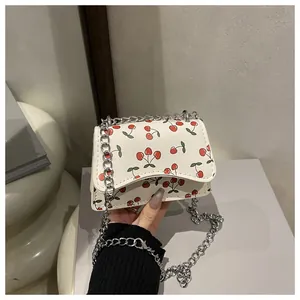 Nahaufnahme der weißen Ledertasche mit Kirschmuster und silbernem Kettenriemen