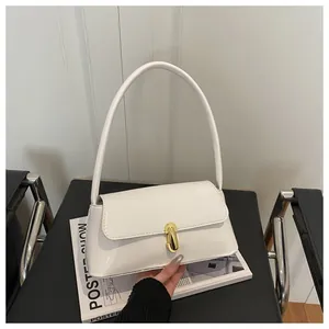 Detailed shot of a white leather baguette bag with a golden oval metal buckle on a magazine