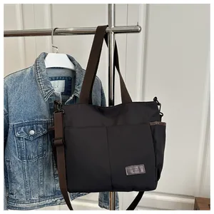 Détail du cabas noir avec anses marron et écusson logo en cuir sur surface en toile