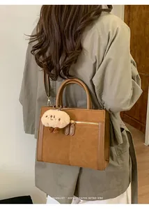 Detalle del bolso tote retro de gamuza marrón con cremallera metálica y colgante de felpa
