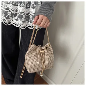 Détail du sac seau tissé avec cordon de serrage, chaîne dorée et perles élégantes