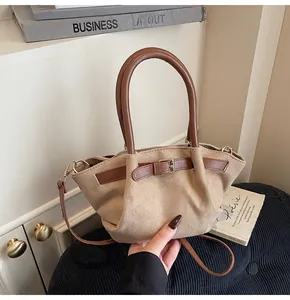 Detail of minimalist beige suede handbag featuring brown leather handles and a strap