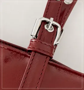 Détail de la boucle de réglage en argent sur un sac bandoulière en cuir verni bordeaux