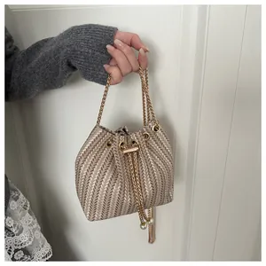 Détail d'un sac seau tissé champagne avec chaîne dorée et perles sur le cordon