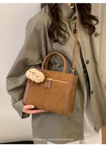 Detalle de bolso tote de ante sintético marrón con cremalleras y peluche decorativo