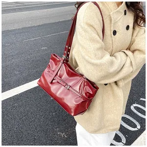 Close-up of a red patent leather shoulder bag with a silver buckle on an outdoor background