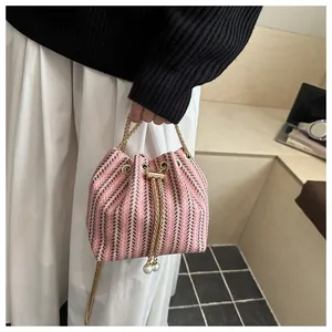 Détail du sac seau tissé à rayures roses, cordon perlé et bandoulière chaîne dorée