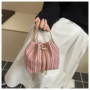 Détail du sac seau tissé rose et noir avec chaîne dorée et perles sur le cordon