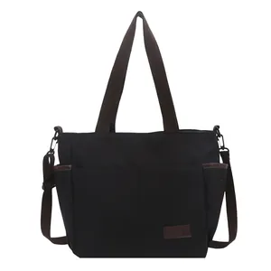 Sac cabas en toile noire avec anses brunes et poches multiples sur un fond blanc neutre