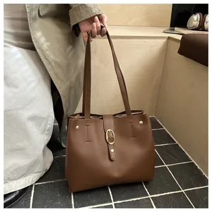 Detail of dark brown tote bag with matte leather and golden metal buckle on a desk