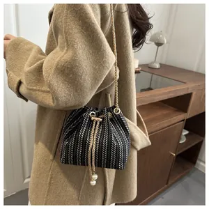 Détail du sac seau tissé avec motif à chevrons, chaîne dorée et cordon en perles