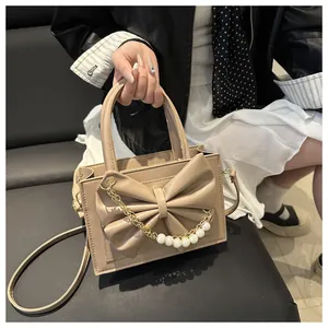 Detail einer beigen Handtasche mit großer Schleife und dekorativer Perlen-Goldkette