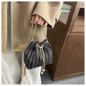 Détail du sac seau tissé avec motif à chevrons, chaîne dorée et breloques en perles au cordon