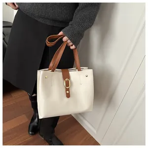 Close-up of cream faux leather tote bag with brown straps and golden metal buckle detail