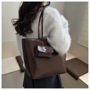 Detail of glossy deep chocolate tote bag with matching mini pouch on a model shoulder