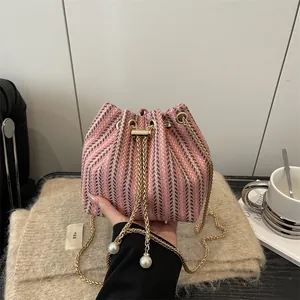 Sac seau tissé rose et gris avec chaîne dorée et détails perlés tenu à la main