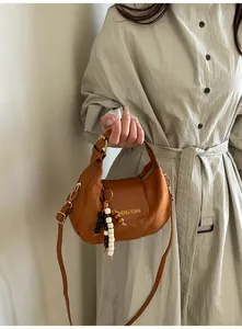 Détail d'un sac à bandoulière en forme de croissant avec textures daim et pompon perlé