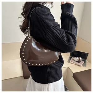 Detail of dark brown glossy crescent bag with gold metal studs shown on shoulder