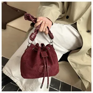 Close-up of burgundy suede bucket bag featuring woven handle and drawstring detail
