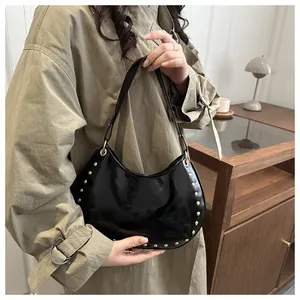 Detail of black glossy leather hobo bag with gold studs on a model in a camel coat