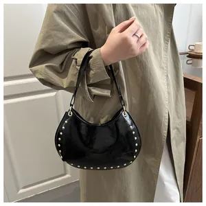 Detailed view of black crescent shoulder bag with golden rivets worn by model in a room
