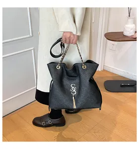 Detalle de bolso bandolera negro con asa de cadena dorada y borla metálica