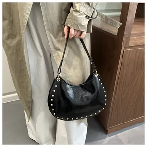Detail of black patent leather hobo bag featuring gold studs and elegant metal rivets