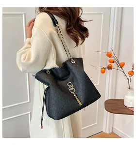 Detalle de bolso tote negro con logo de dólar dorado, flecos y correa de cadena metal