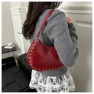 Detail of red crescent shoulder bag featuring gold studs and slim leather strap