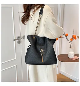 Detalle de bolso en cuero negro con logo SS dorado, borla de flecos y correa de cadena
