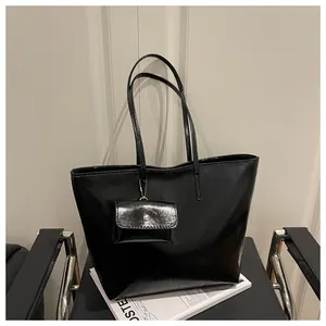 Close-up of glossy black tote bag with matching mini coin purse on a modern chair