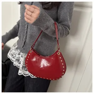 Detailed shot of red crescent bag with glossy patent leather and gold rivet studs