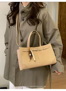 Detail of khaki woven tote bag with leather straps and wooden bead charm accessory