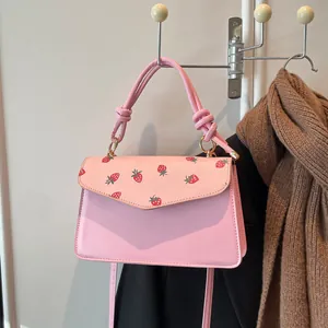 Pink strawberry print crossbody bag with knotted handle hanging on a white rack